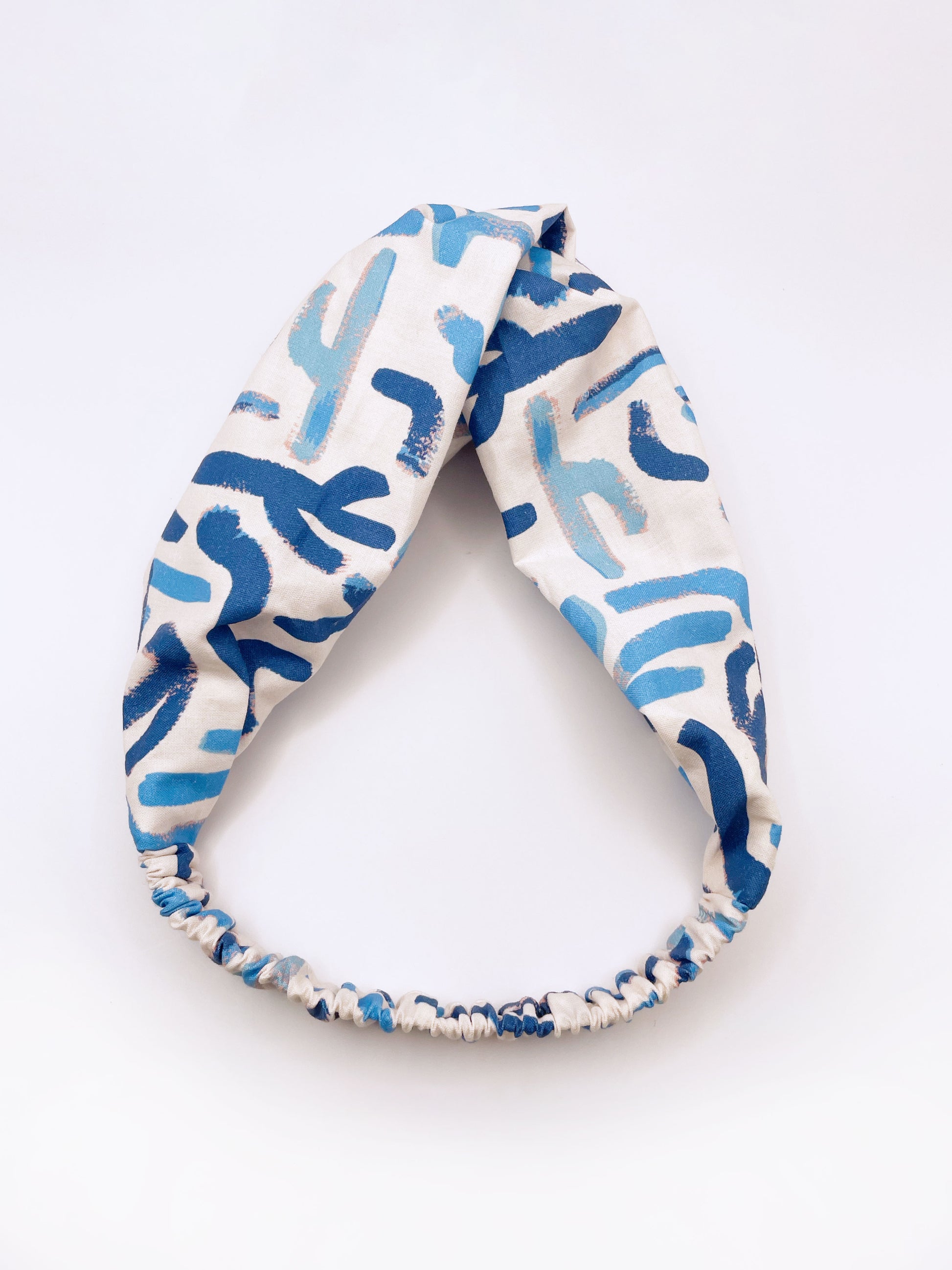A twist headband featuring a bold blue cactus print. The headband has an elastic band on the back.