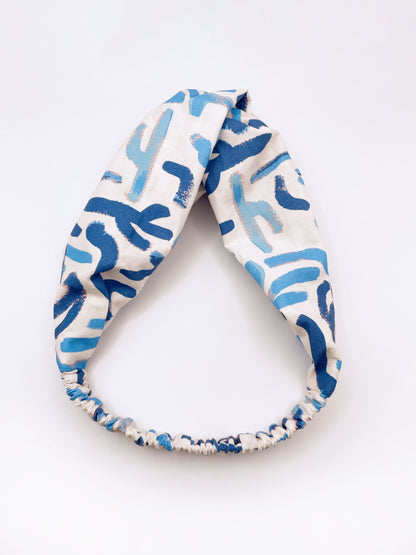 A twist headband featuring a bold blue cactus print. The headband has an elastic band on the back.
