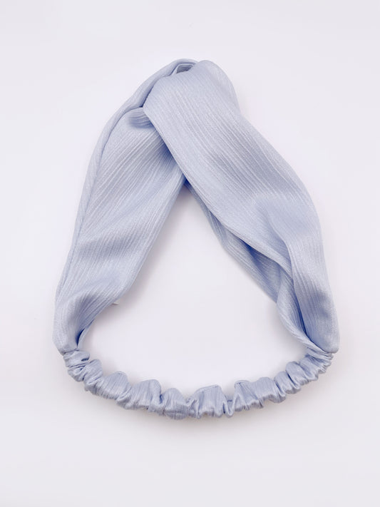 A twist headband made with a light sky blue crinkle satin fabric. The headband has an elastic band in the back.