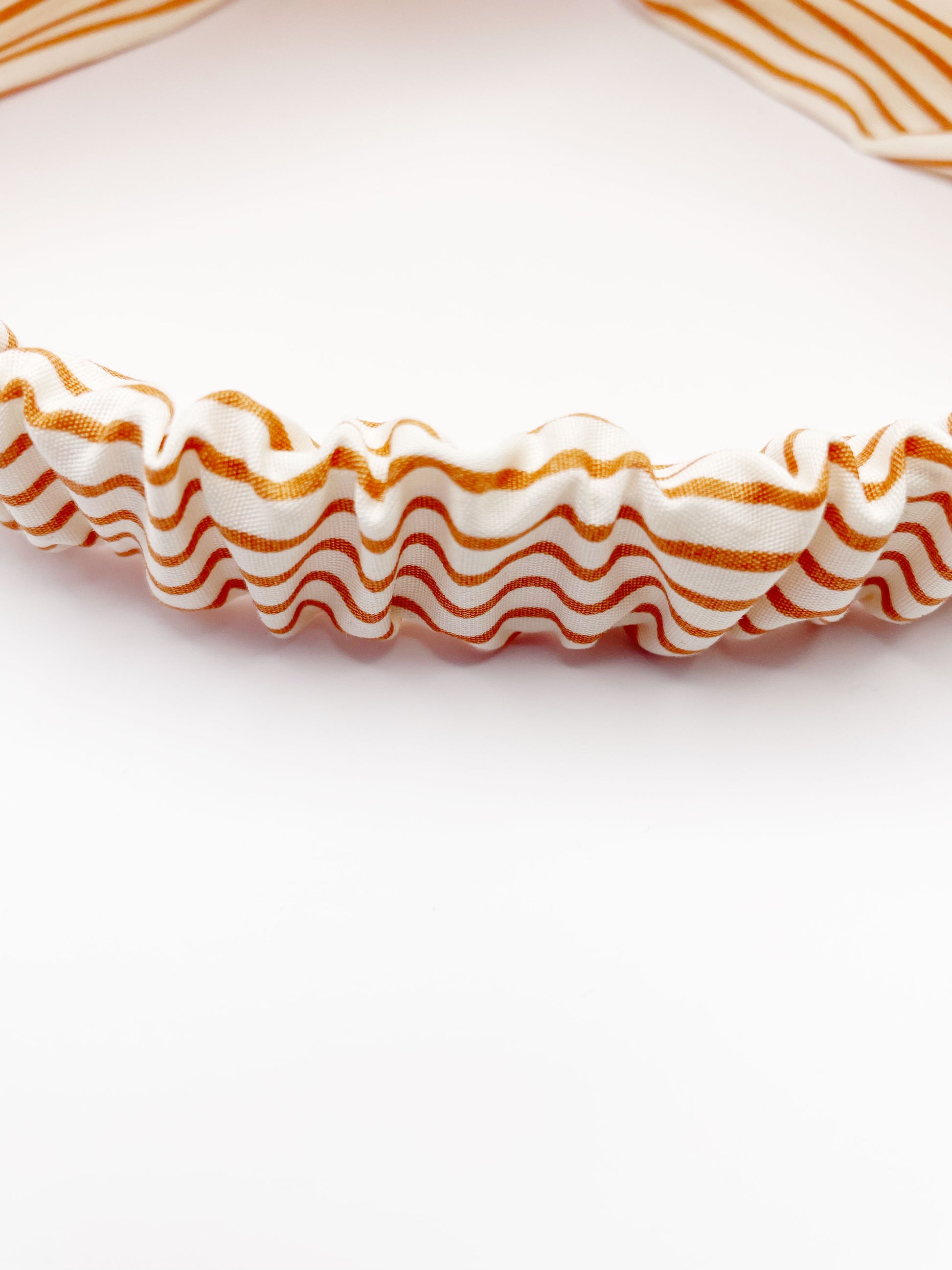 A handmade tan striped twist headband with an elastic band in the back.