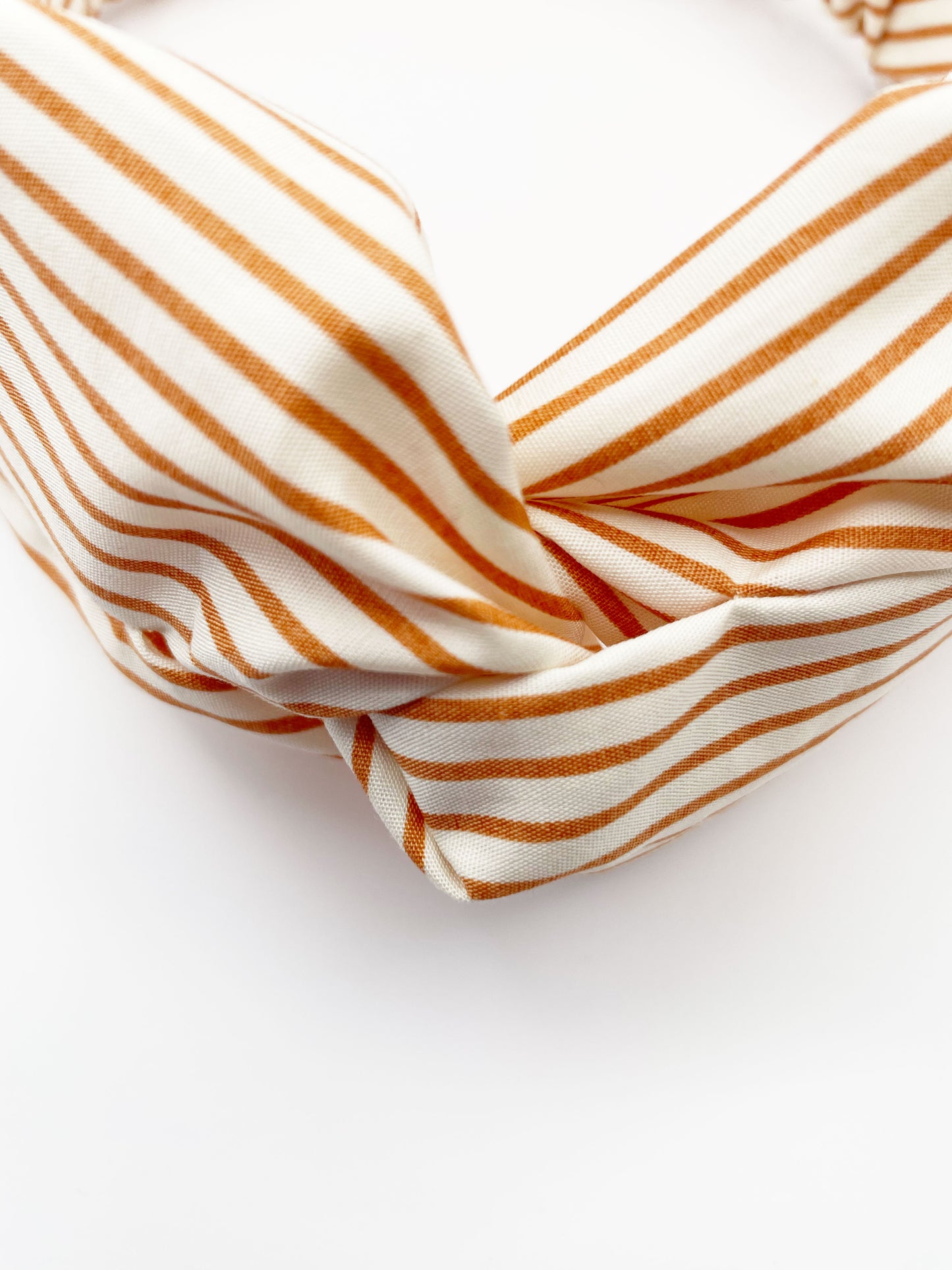 A handmade tan striped twist headband with an elastic band in the back.