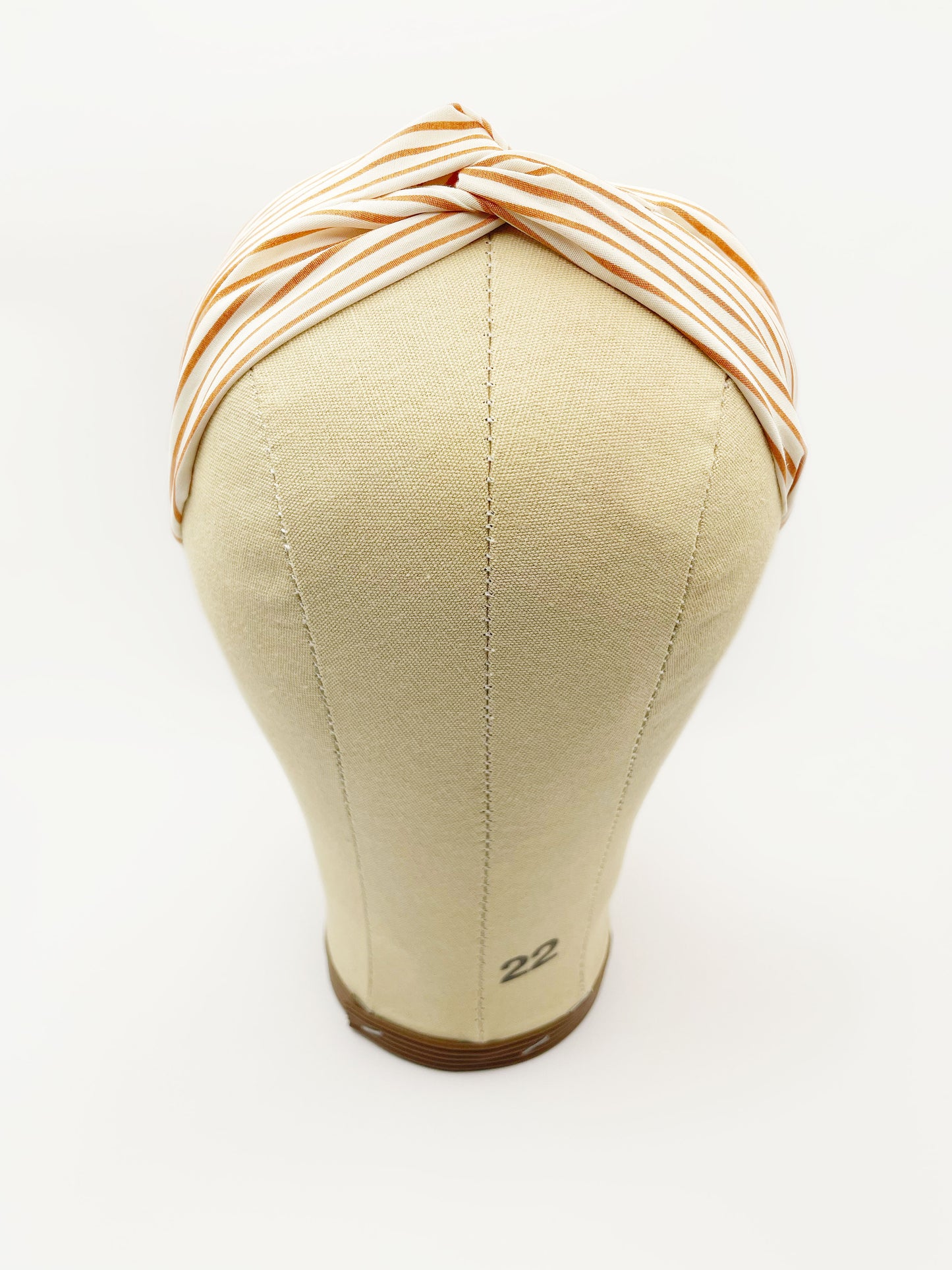 A handmade tan striped twist headband with an elastic band in the back. The headband is modeled on a mannequin head.