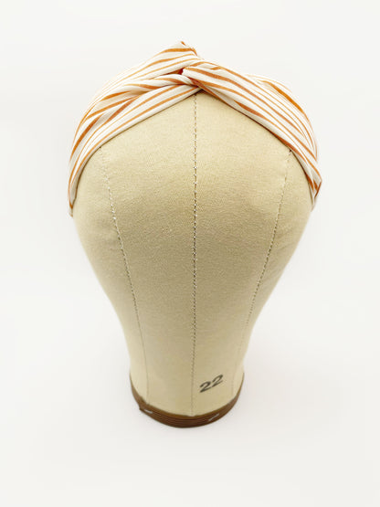 A handmade tan striped twist headband with an elastic band in the back. The headband is modeled on a mannequin head.