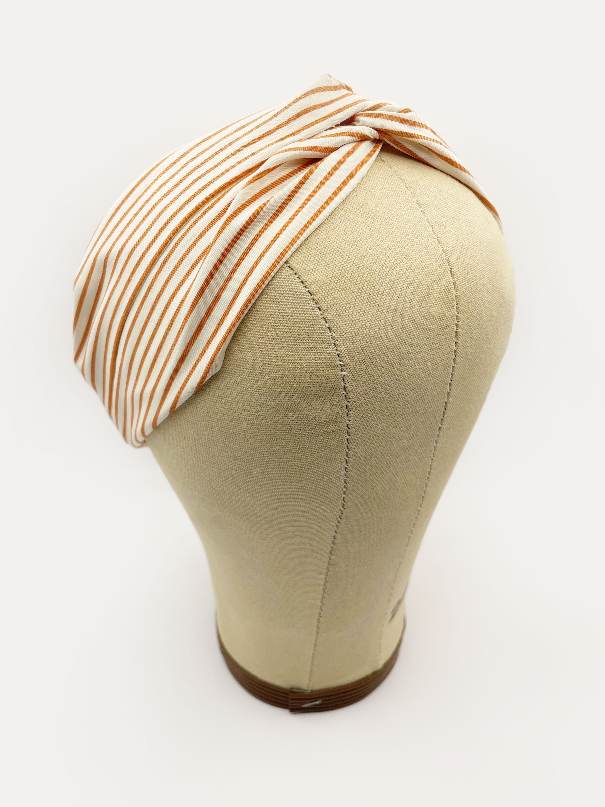 A handmade tan striped twist headband with an elastic band in the back. The headband is modeled on a mannequin head.