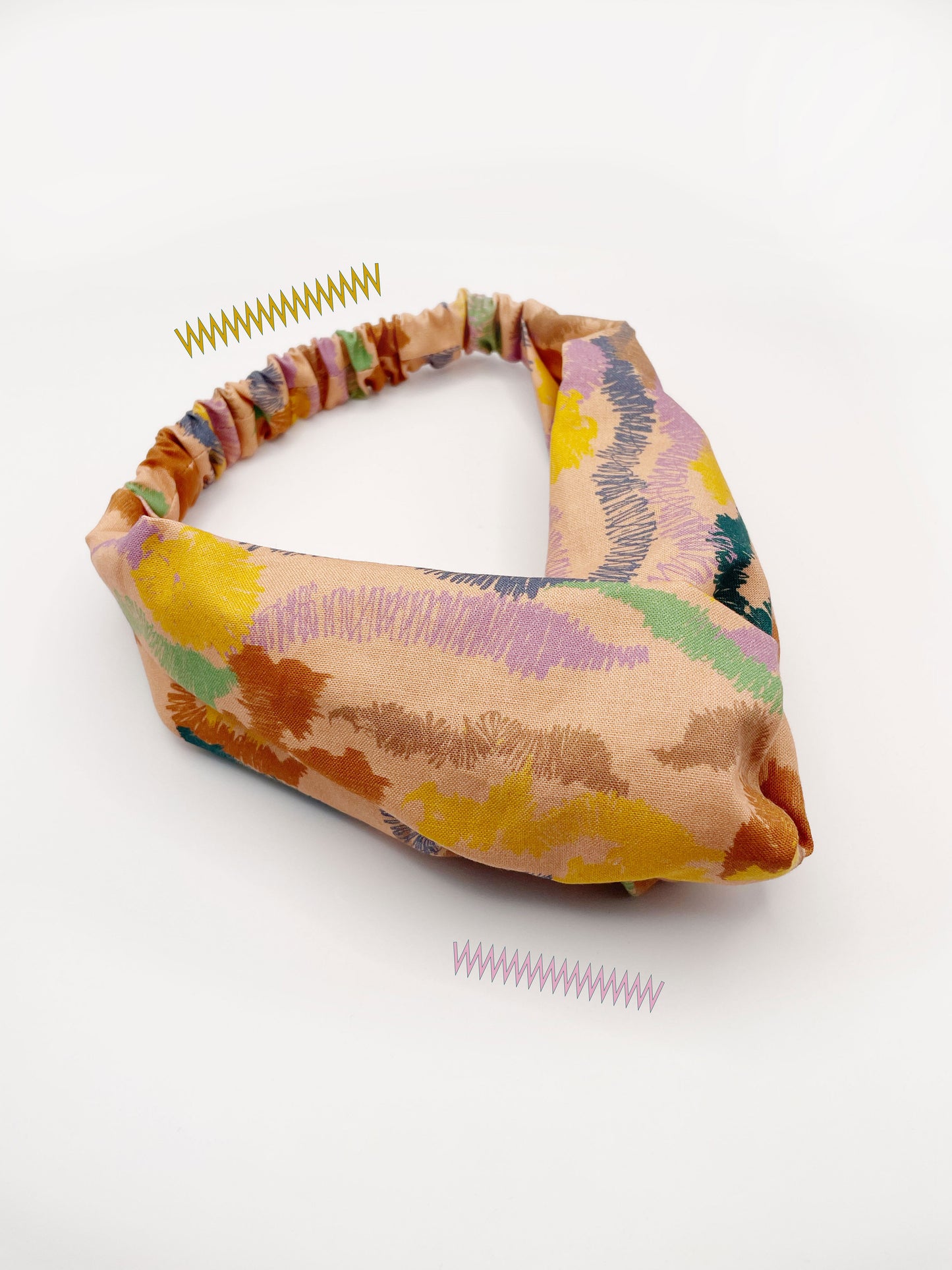 A twist headband crafted from high-quality cotton with an abstract design inspired by the rolling hills and earthy tones of the desert. The headband has an elastic band in the back.