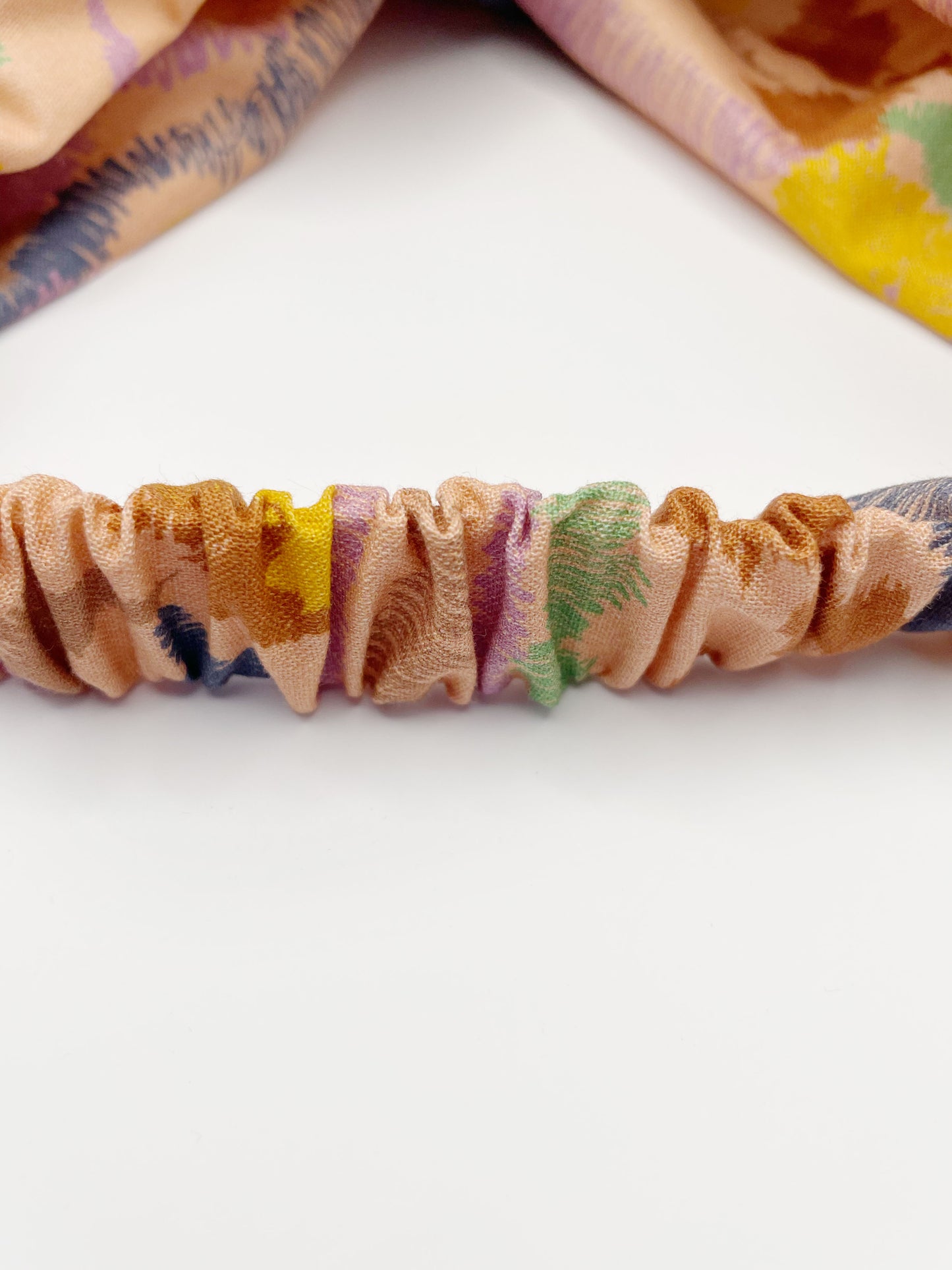 A twist headband crafted from high-quality cotton with an abstract design inspired by the rolling hills and earthy tones of the desert. The headband has an elastic band in the back.