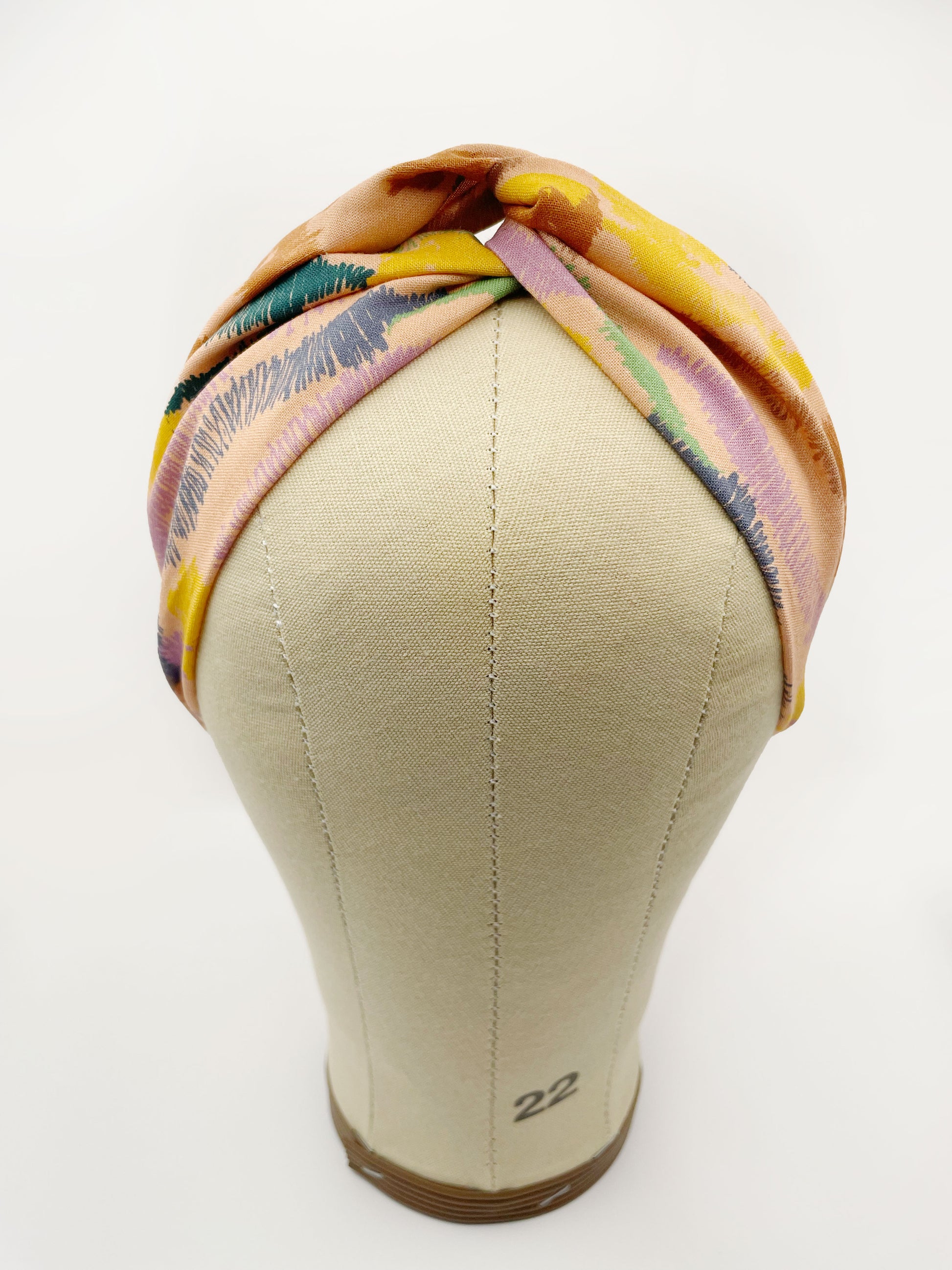 A twist headband crafted from high-quality cotton with an abstract design inspired by the rolling hills and earthy tones of the desert. The headband is shown on a mannequin head.