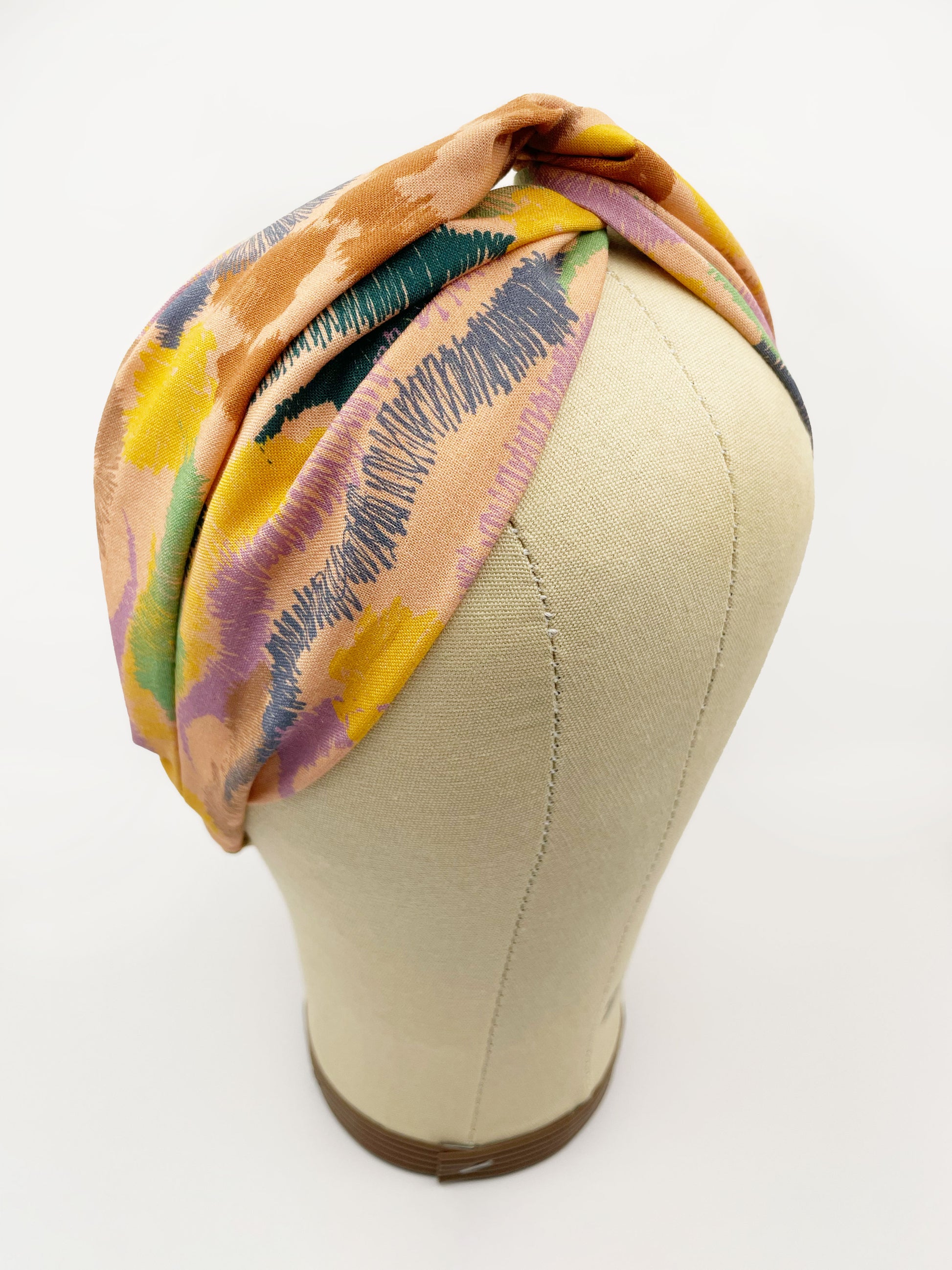 A twist headband crafted from high-quality cotton with an abstract design inspired by the rolling hills and earthy tones of the desert. The headband is shown on a mannequin head.