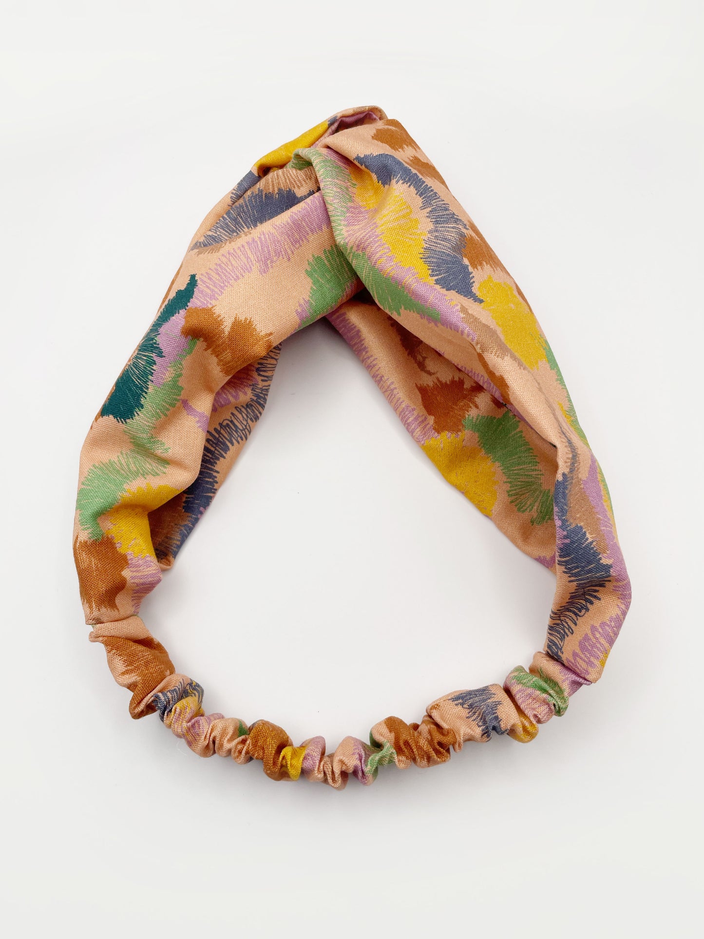 A twist headband crafted from high-quality cotton with an abstract design inspired by the rolling hills and earthy tones of the desert. The headband has an elastic band in the back.