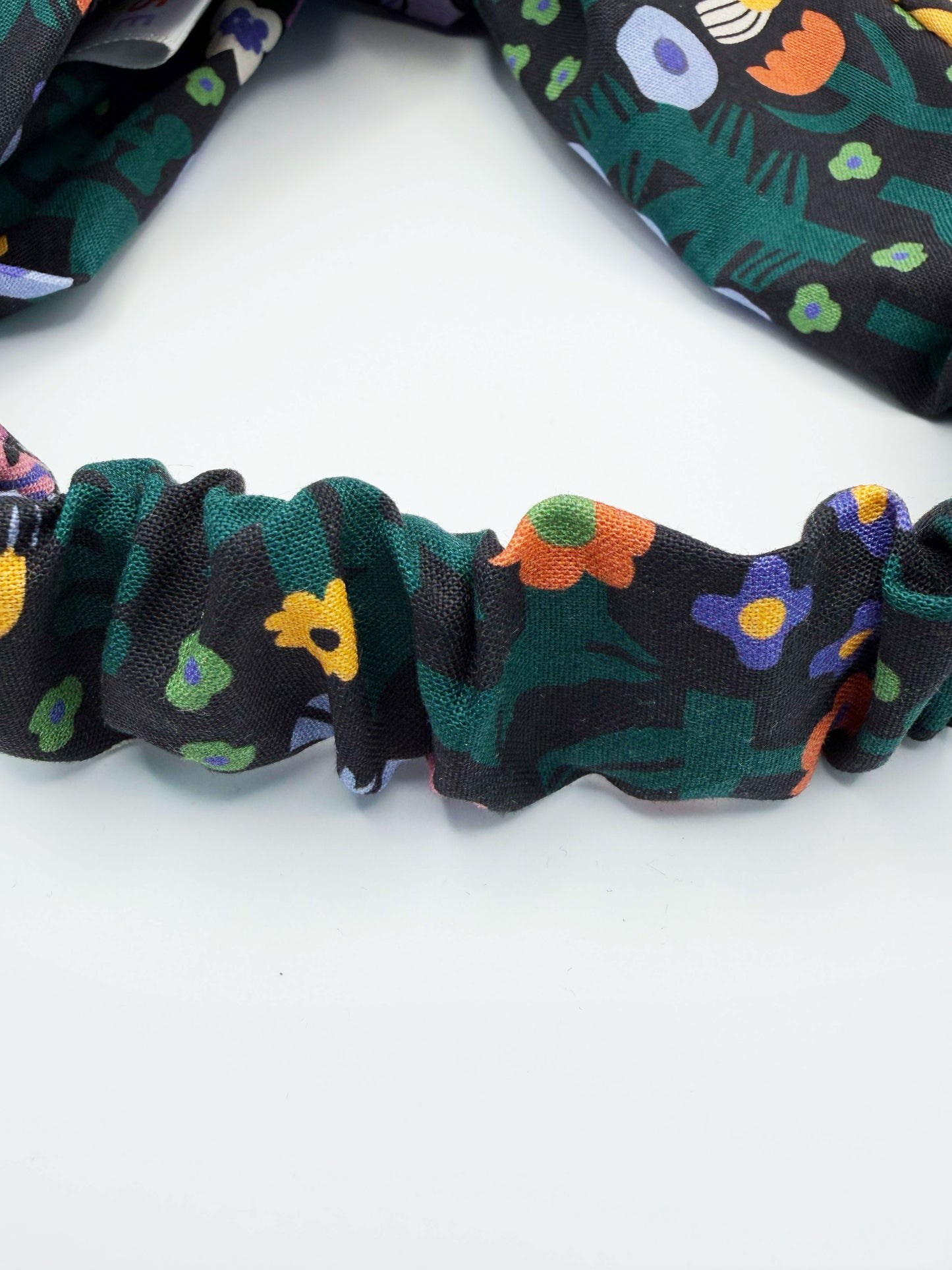 A black twist headband with a colorful abstract forest print featuring playful florals, leaves, and bright animals. The headband has an elastic band on the back.