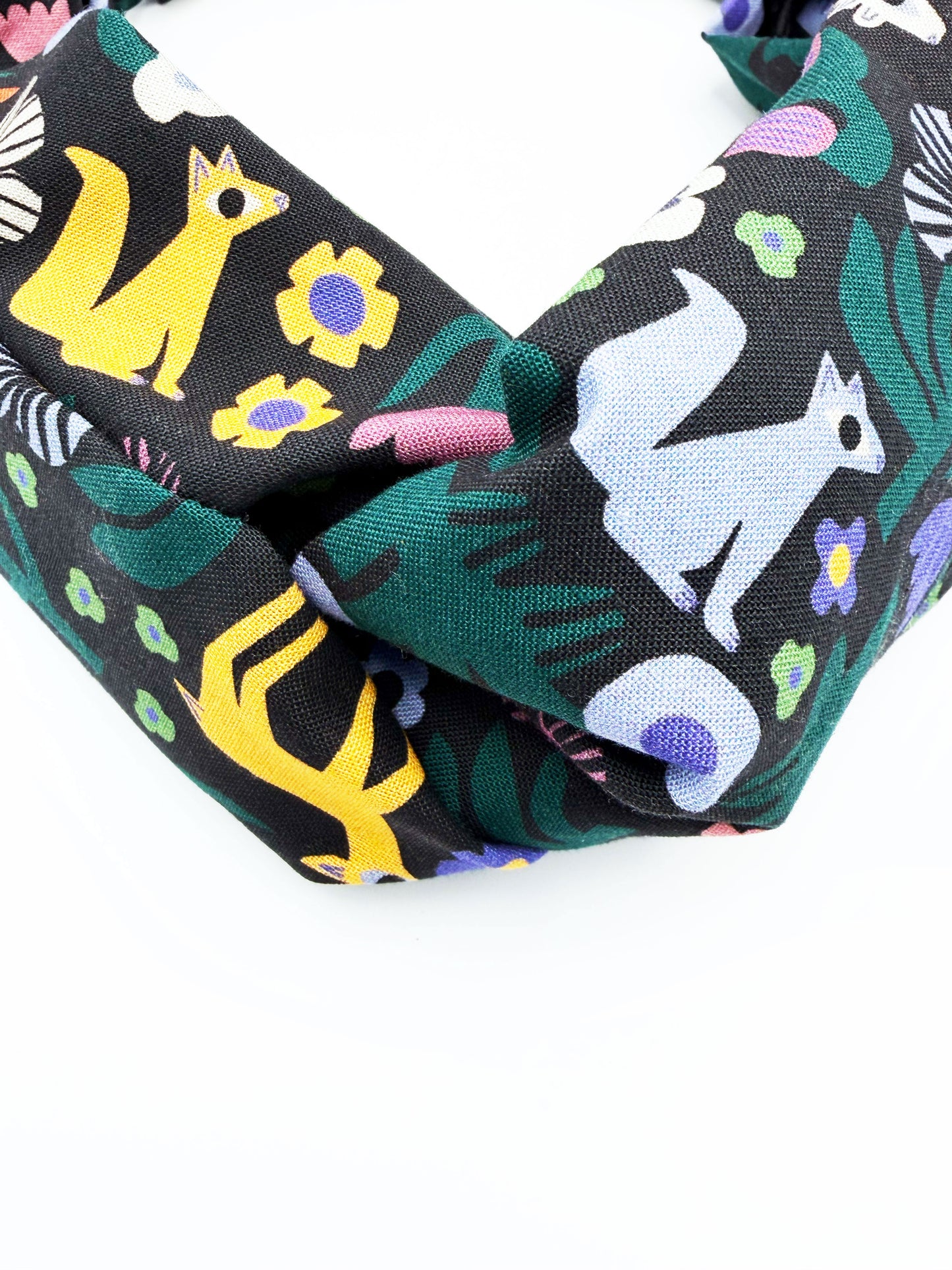 A black twist headband with a colorful abstract forest print featuring playful florals, leaves, and bright animals.
