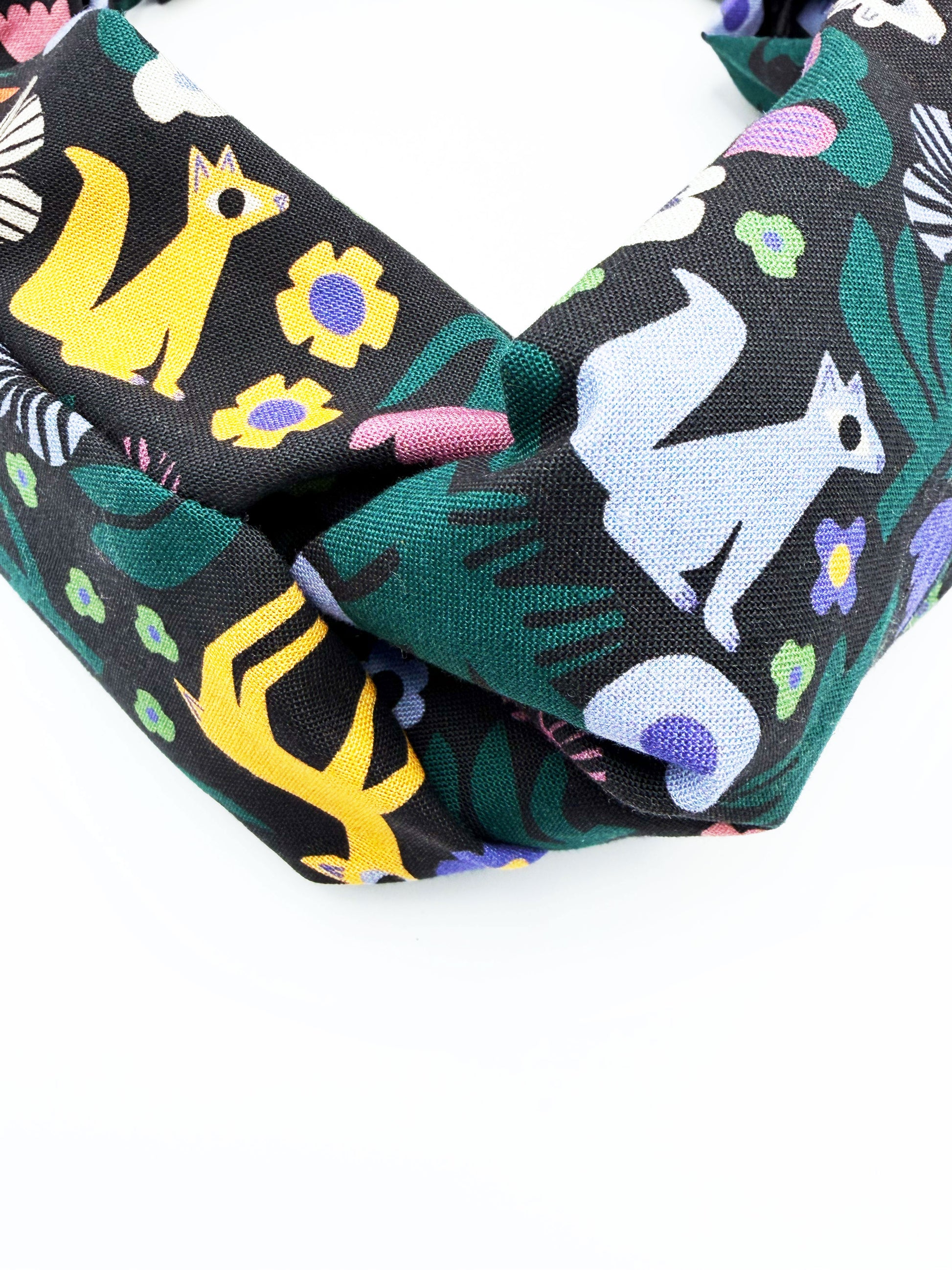 A black twist headband with a colorful abstract forest print featuring playful florals, leaves, and bright animals.