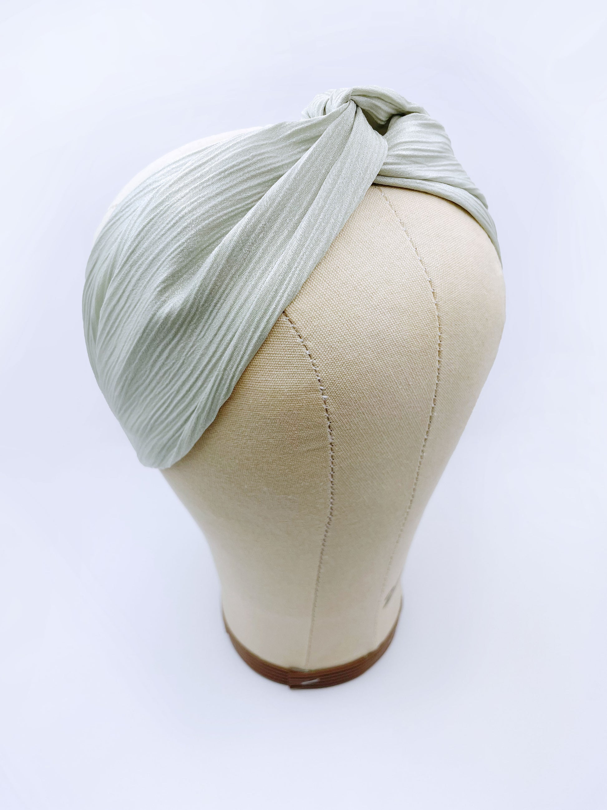 A twist headband made with a pastel green crinkle satin fabric. The headband is on a mannequin head.