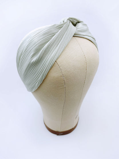 A twist headband made with a pastel green crinkle satin fabric. The headband is on a mannequin head.