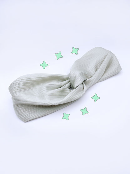 A twist headband made with a pastel green crinkle satin fabric.