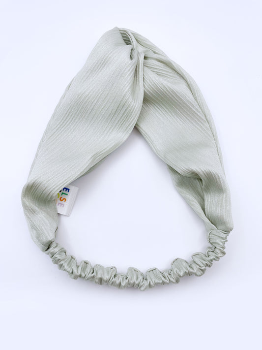 A twist headband made with a pastel green crinkle satin fabric. The headband has an elastic band in the back.