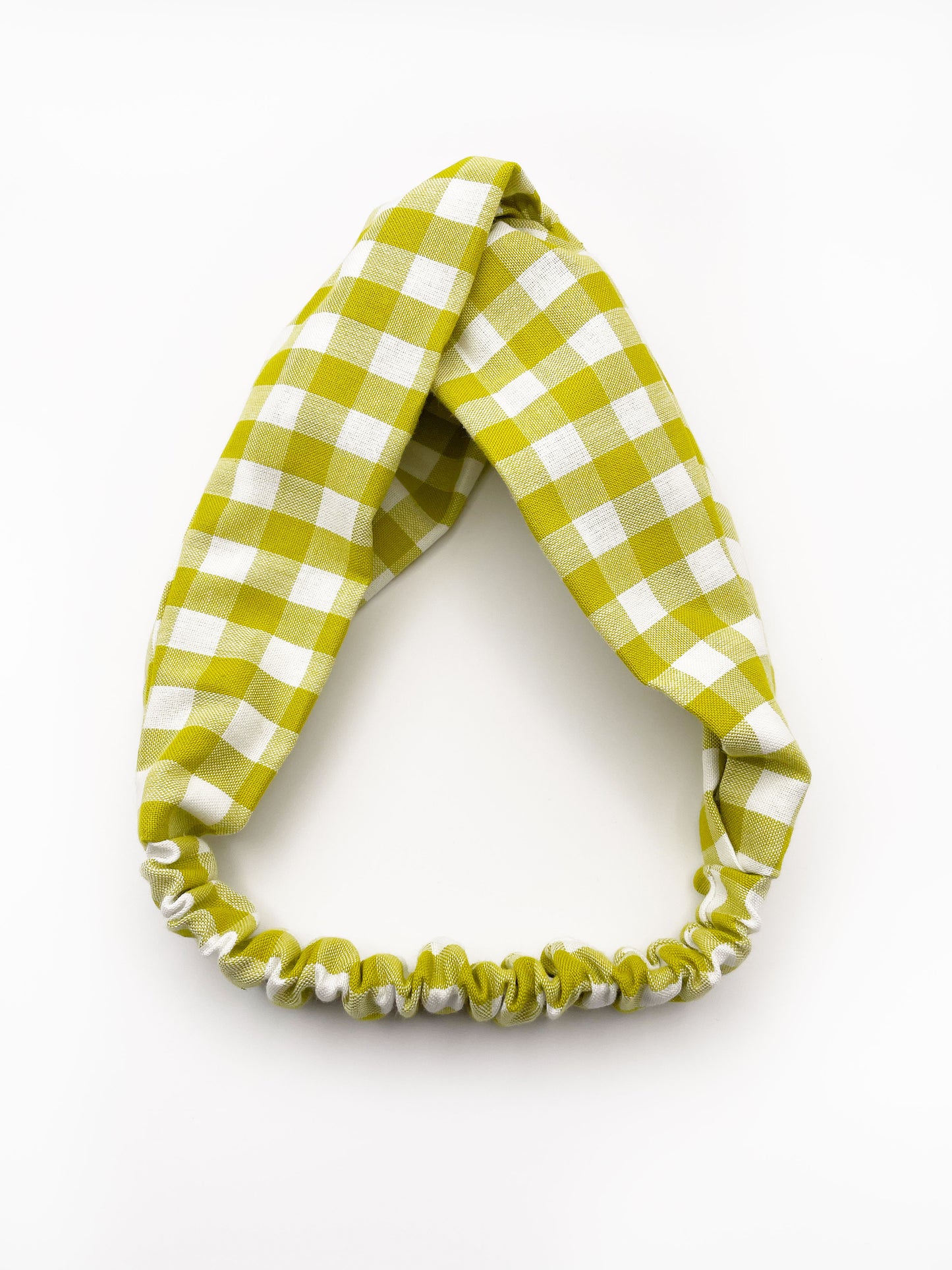 A handmade twist headband with a green and white gingham plaid print. The headband has an elastic band in the back. 