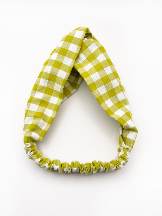A handmade twist headband with a green and white gingham plaid print. The headband has an elastic band in the back. 