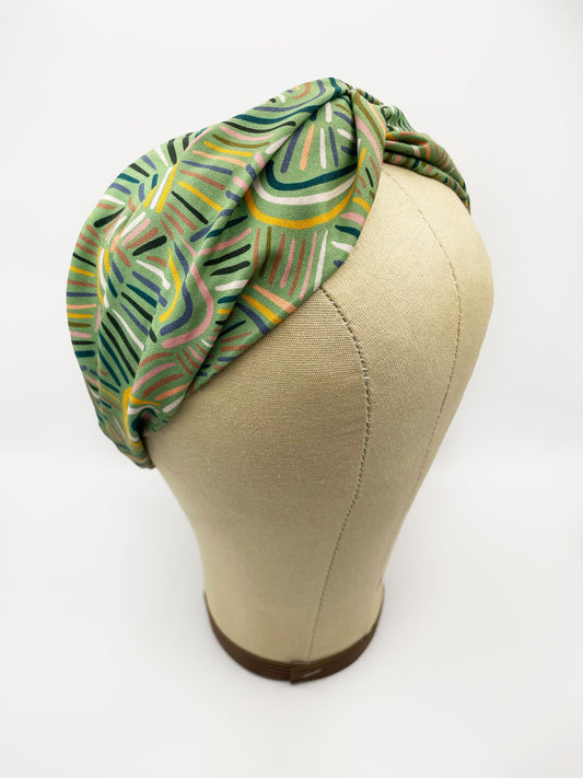 A twist headband made from high-quality cotton with an abstract design inspired by desert rain patterns. The headband is shown on a mannequin head.