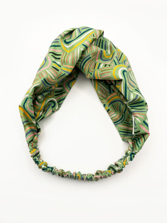 A twist headband made from high-quality cotton with an abstract design inspired by desert rain patterns. The headband has an elastic band in the back.