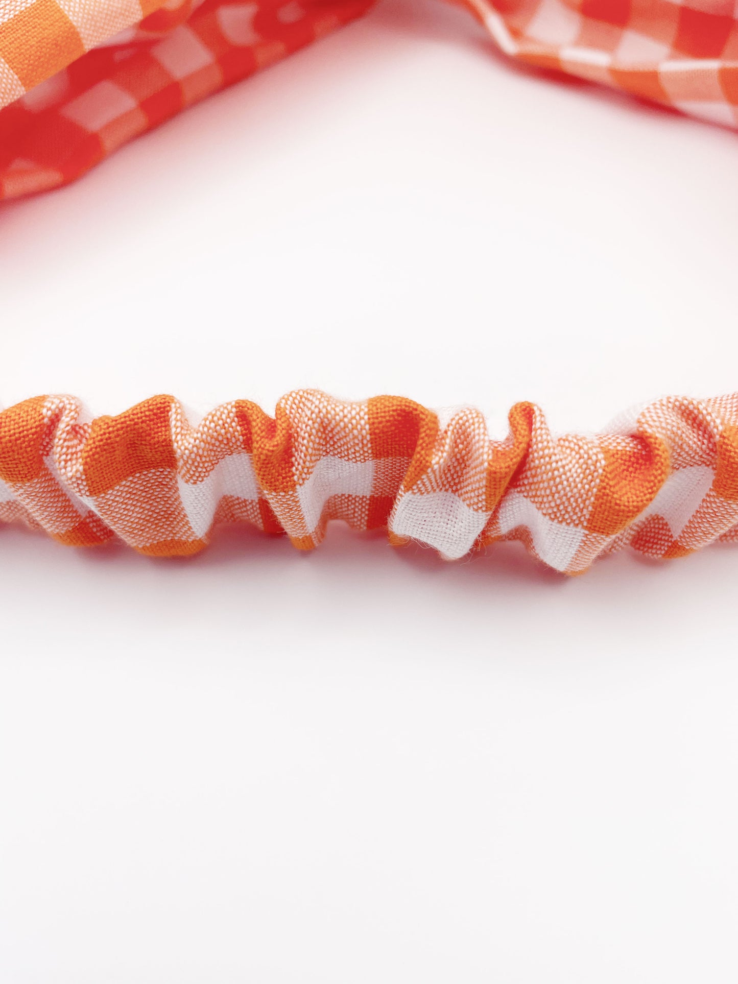 A handmade orange and white gingham plaid twist headband with an elastic band in the back.