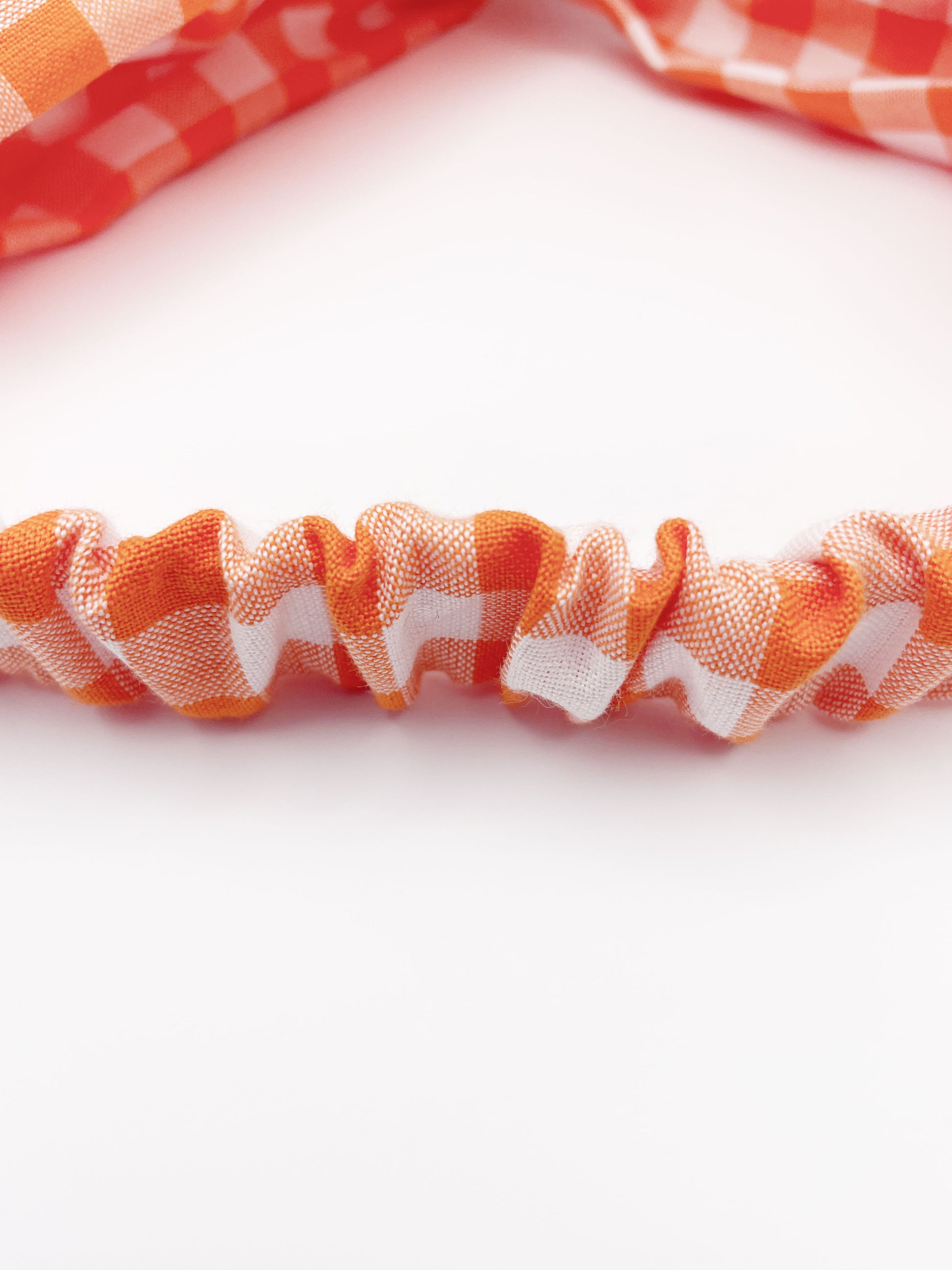 A handmade orange and white gingham plaid twist headband with an elastic band in the back.