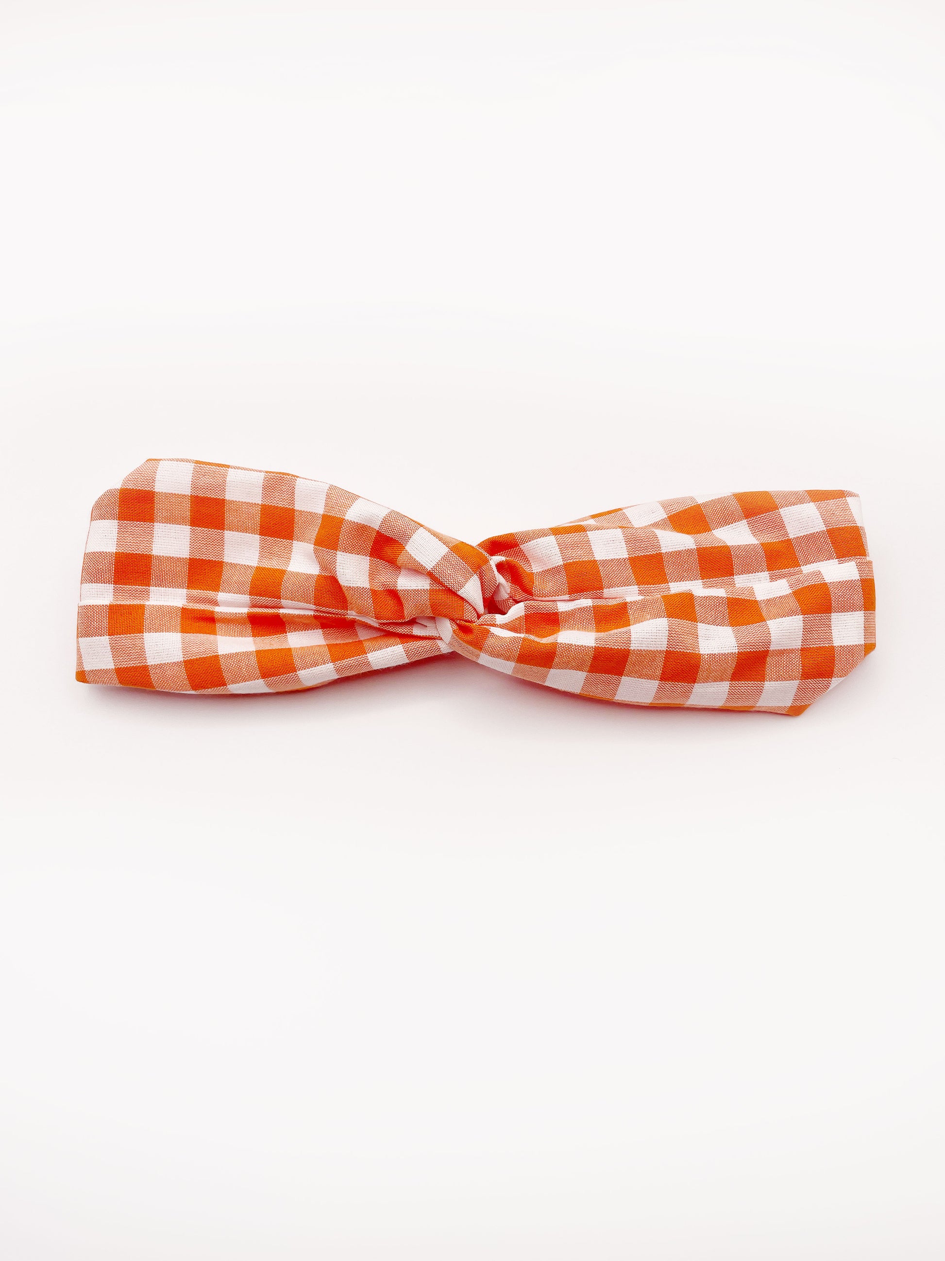 A handmade orange and white gingham plaid twist headband with an elastic band in the back.