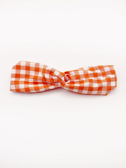 A handmade orange and white gingham plaid twist headband with an elastic band in the back.