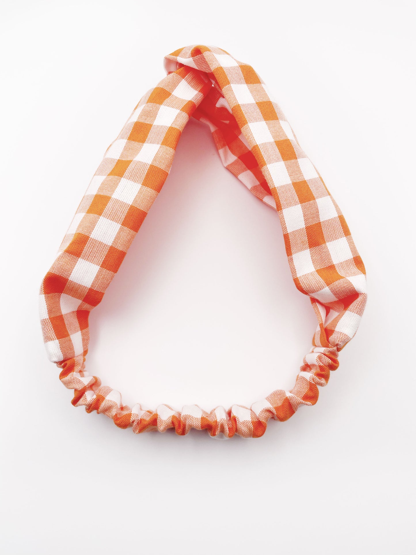 A handmade orange and white gingham plaid twist headband with an elastic band in the back.