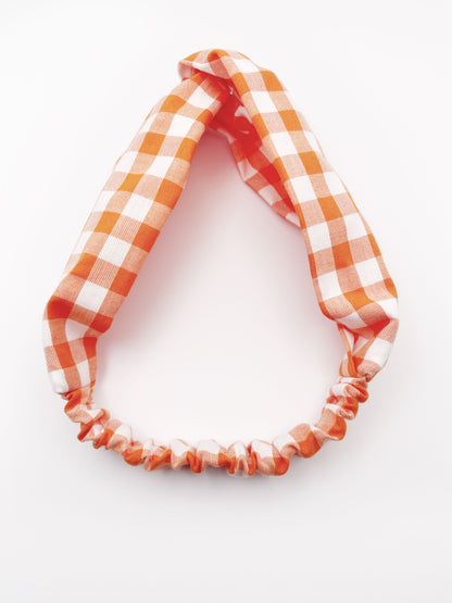 A handmade orange and white gingham plaid twist headband with an elastic band in the back.