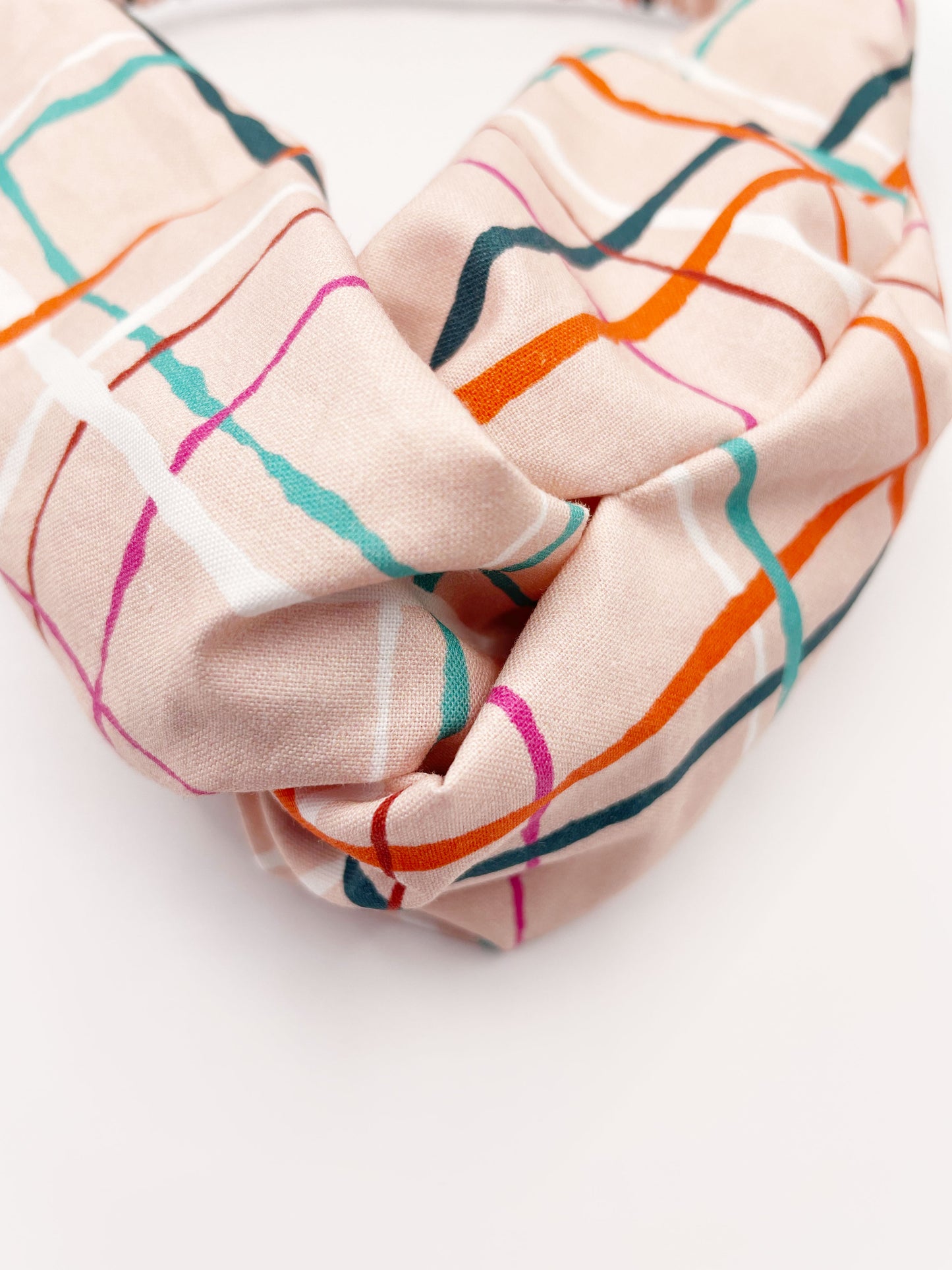 A fabric headband featuring a colorful and modern plaid design with vibrant shades of pink, red, teal, and orange on a soft pastel background. 