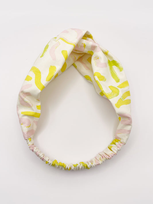 A twist headband featuring a yellow cactus print with hints of pink and green. The headband has an elastic band in the back.