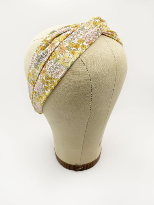 A handmade yellow floral twist headband with an elastic band in the back. The headband is modeled on a mannequin head.