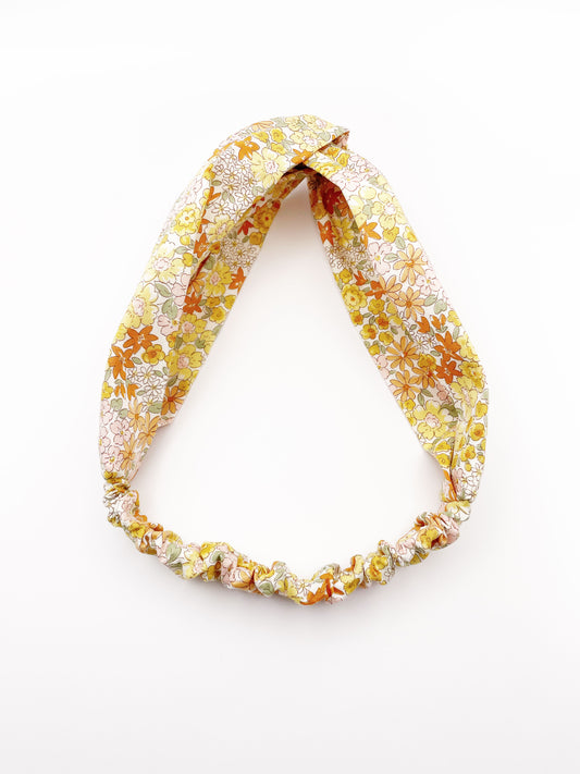 A handmade yellow floral twist headband with an elastic band in the back.