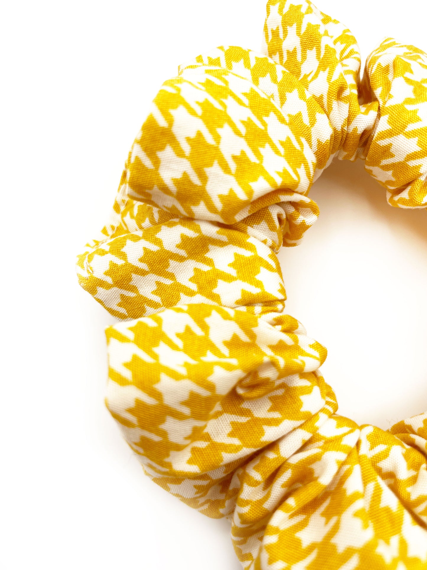 A handmade scrunchie made with cotton fabric featuring a cheerful yellow houndstooth print.