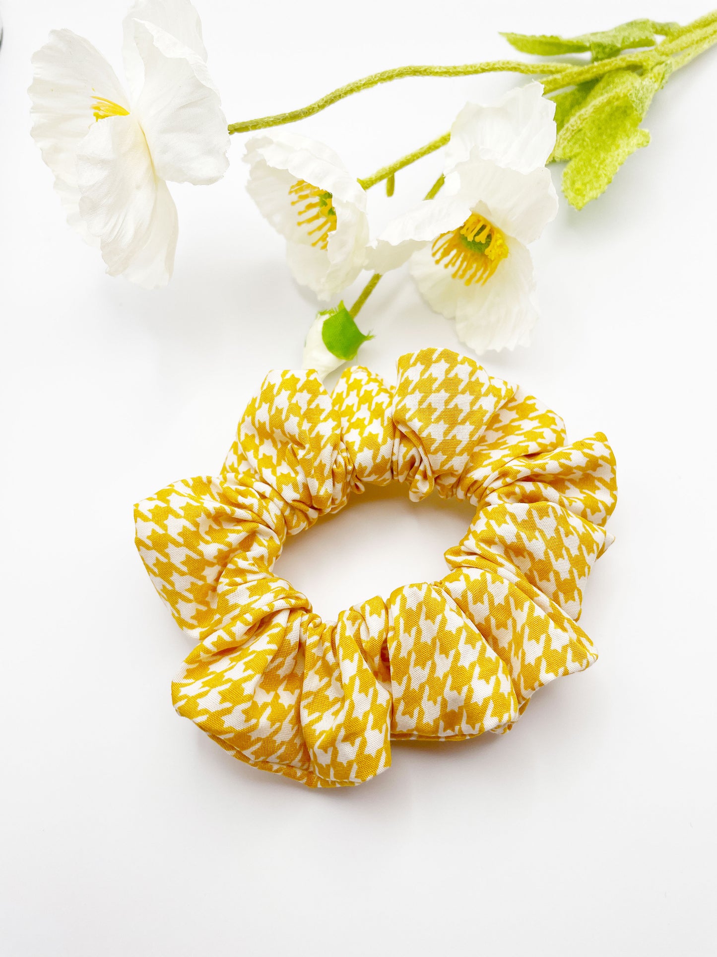 A handmade scrunchie made with cotton fabric featuring a cheerful yellow houndstooth print.