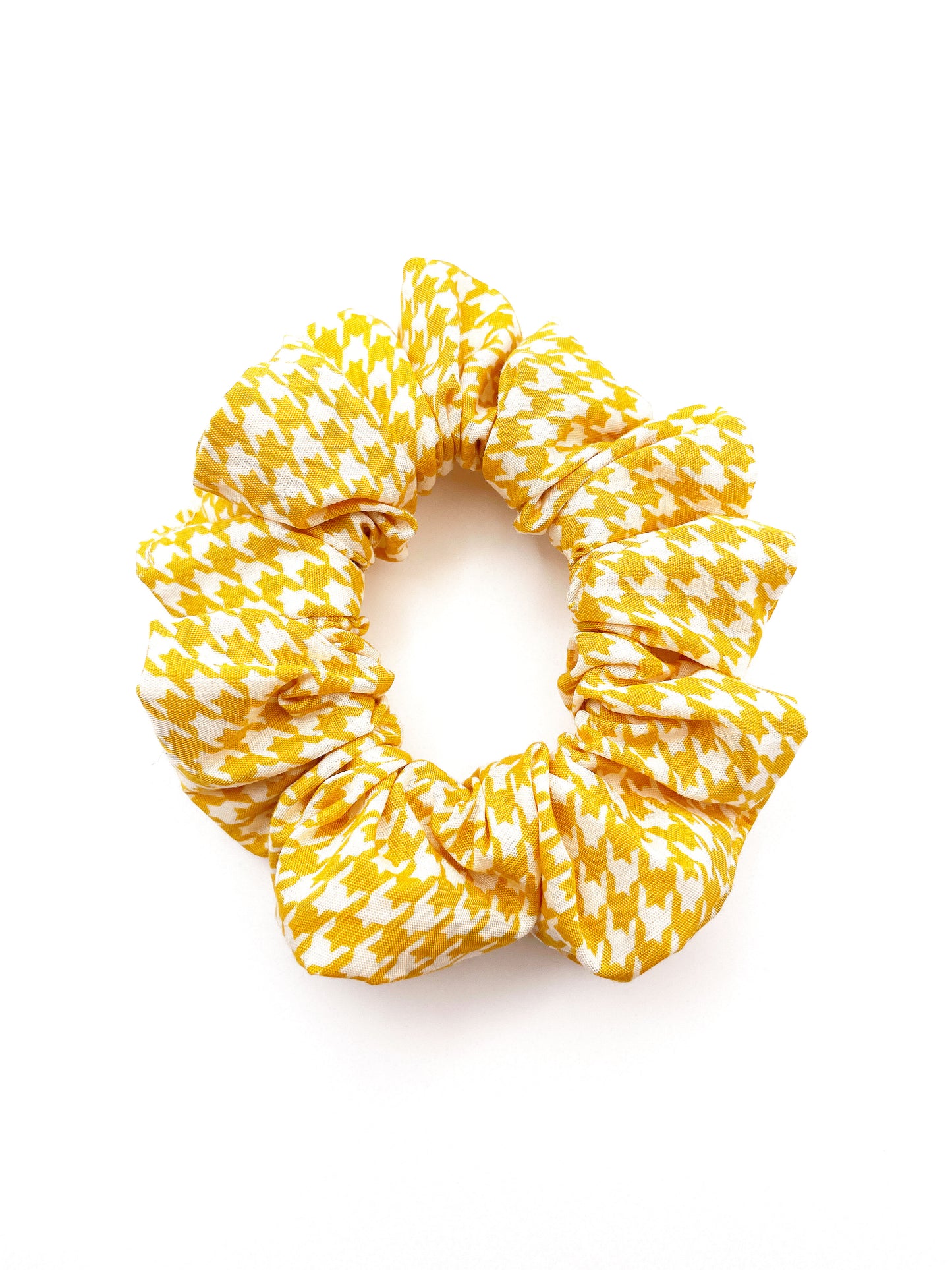 A handmade scrunchie made with cotton fabric featuring a cheerful yellow houndstooth print.