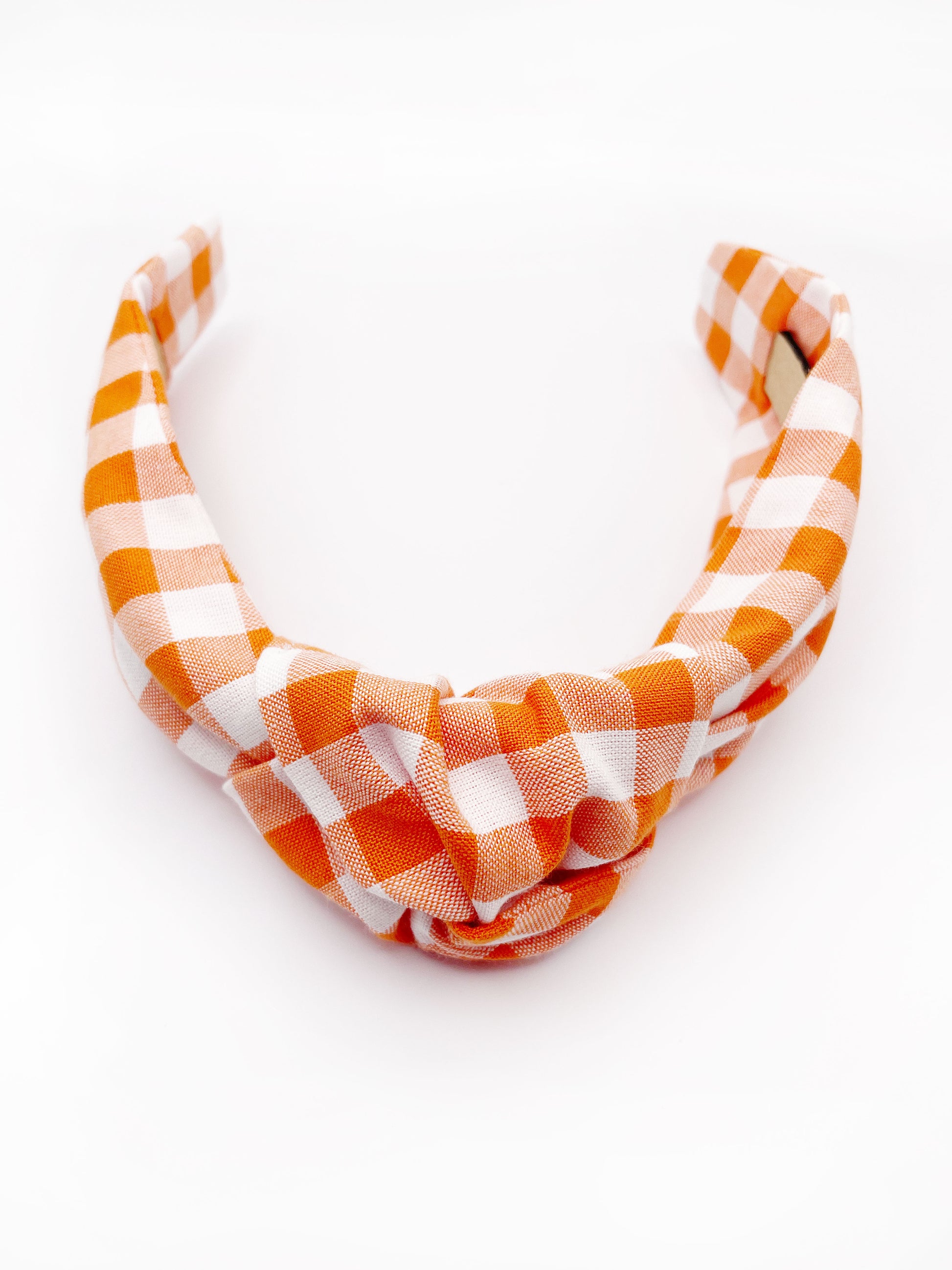 A knotted headband with an orange and white gingham plaid print. 