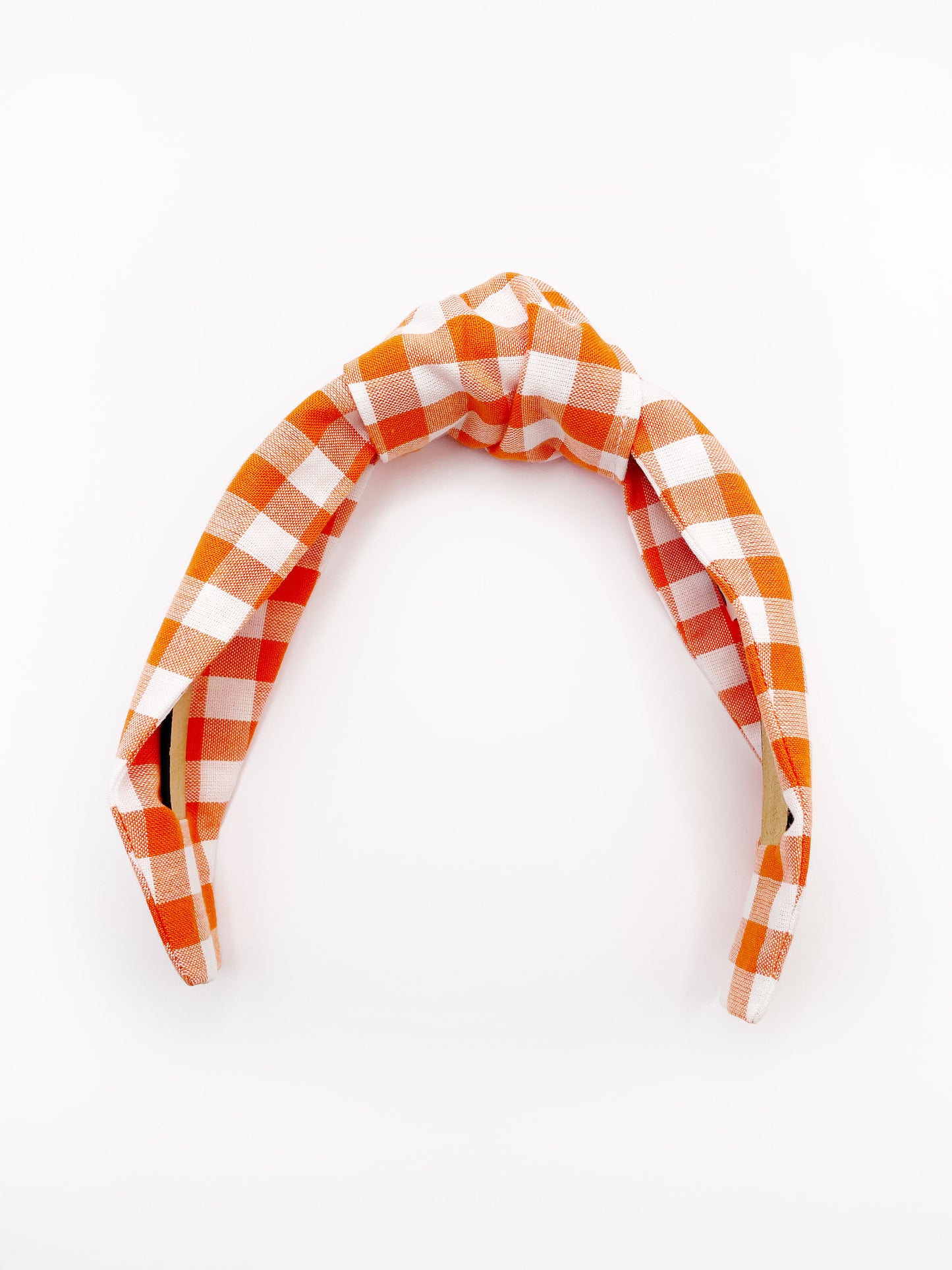 A knotted headband with an orange and white gingham plaid print. 