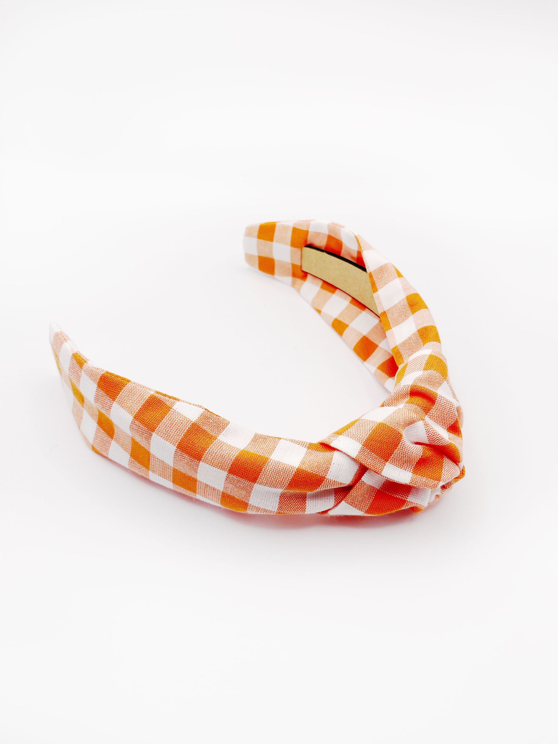 A knotted headband with an orange and white gingham plaid print. 