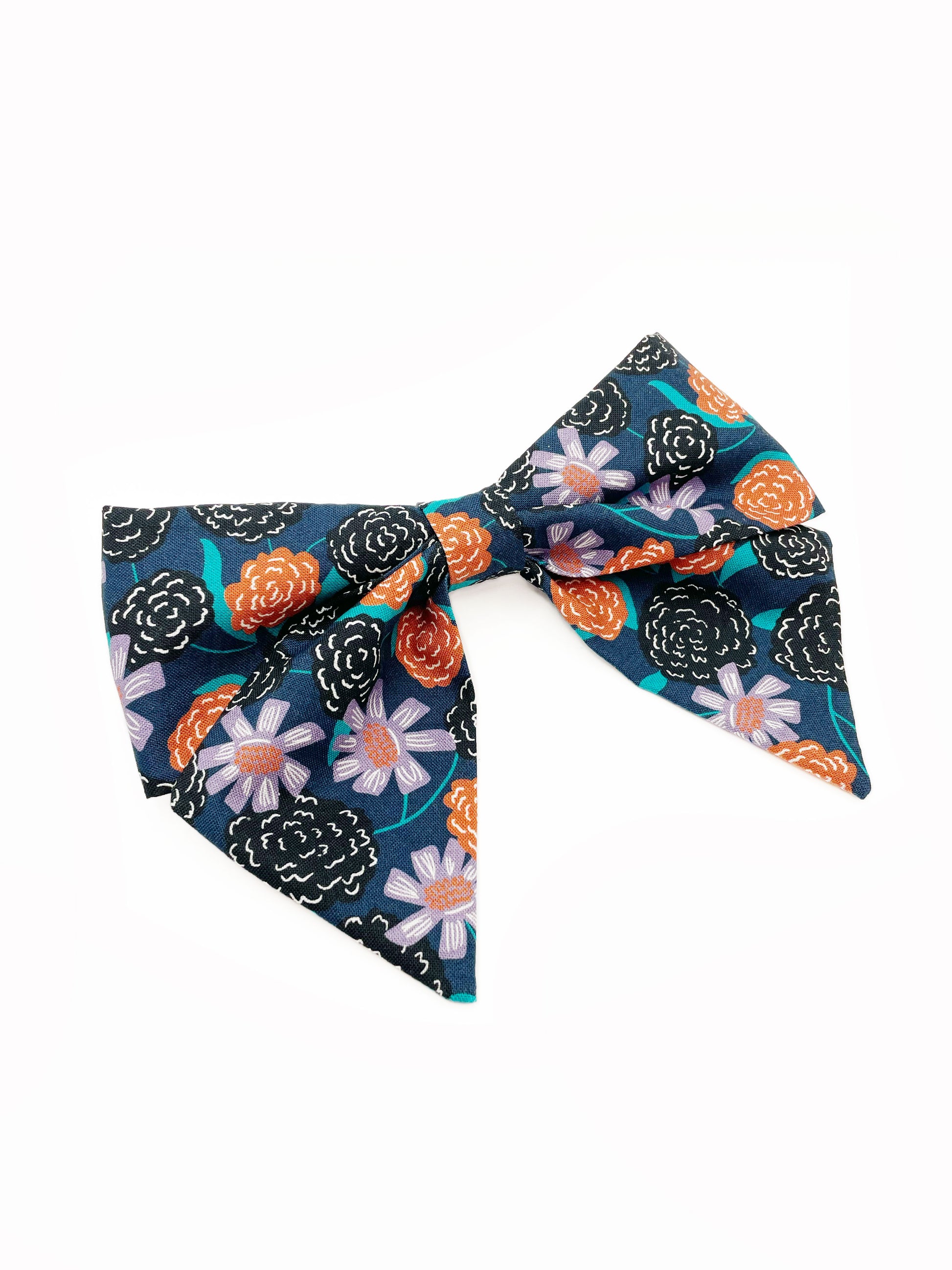 A large handmade hair bow with vivid orange, lavender, and black flowers, accented with fresh green leaves. The cotton fabric is attached to a sturdy barrette clip.