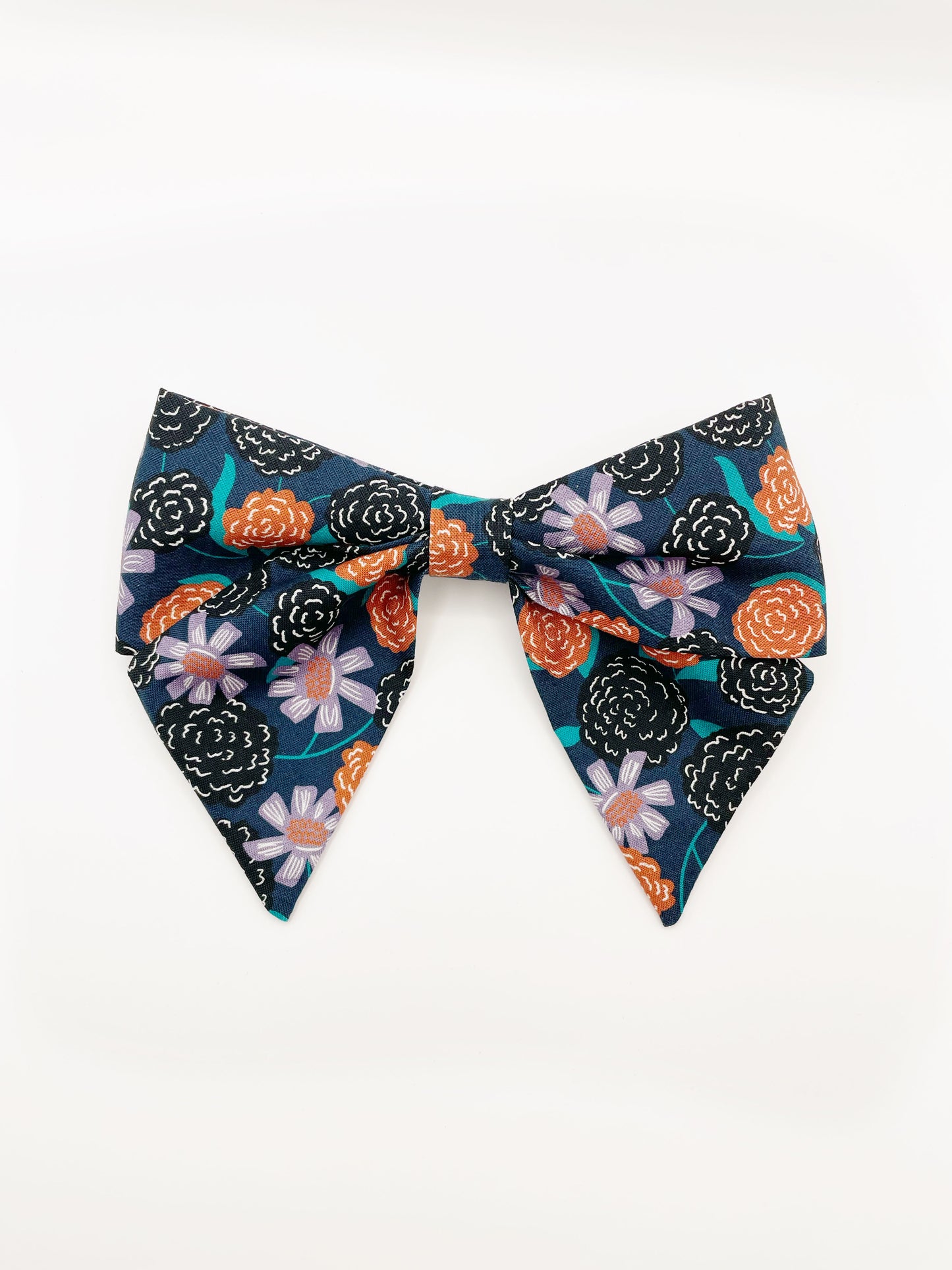 A large handmade hair bow with vivid orange, lavender, and black flowers, accented with fresh green leaves.