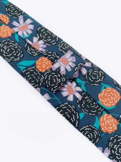 A navy blue necktie with vivid orange, lavender, and black flowers, accented with fresh green leaves.