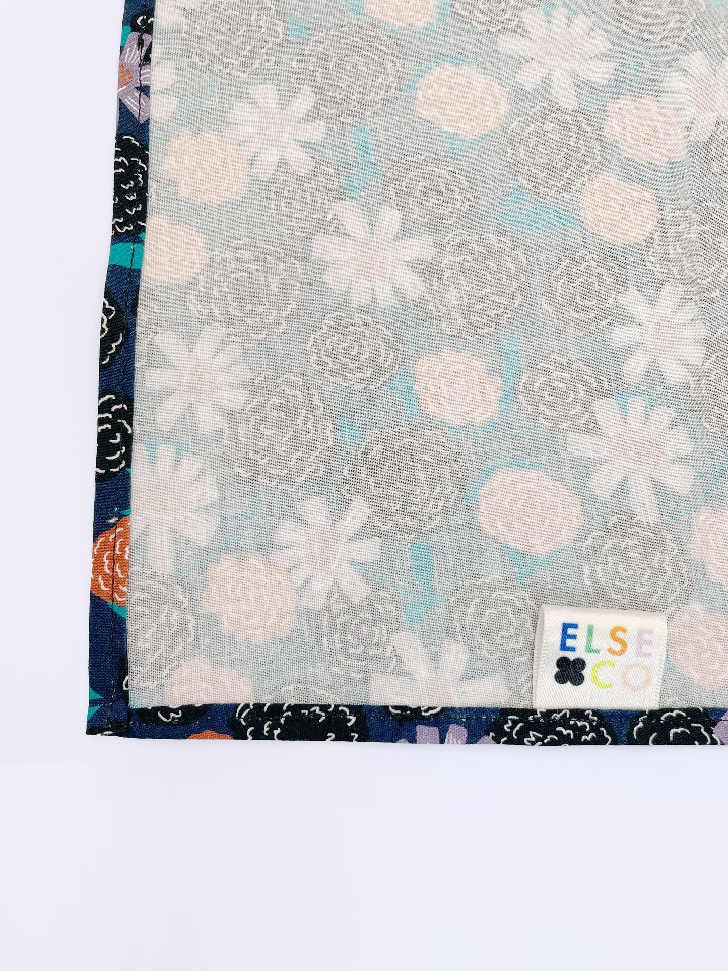 A navy blue pocket square with vivid orange, lavender, and black flowers, accented with fresh green leaves.