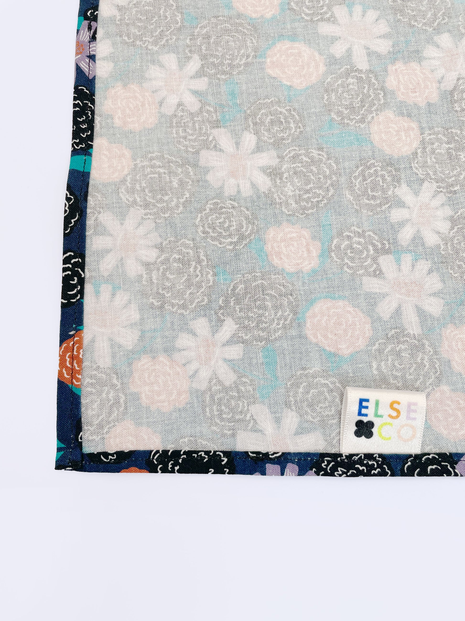 A navy blue pocket square with vivid orange, lavender, and black flowers, accented with fresh green leaves.