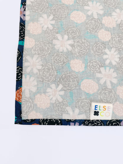 A navy blue pocket square with vivid orange, lavender, and black flowers, accented with fresh green leaves.
