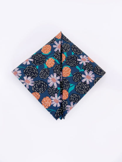 A navy blue pocket square with vivid orange, lavender, and black flowers, accented with fresh green leaves.