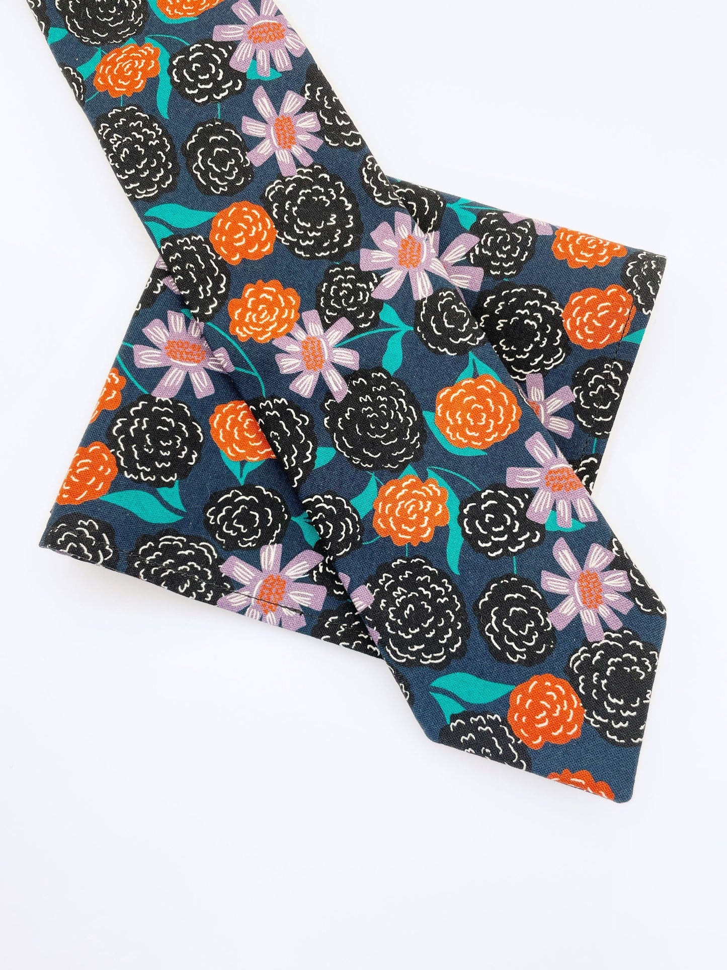 A navy blue pocket square with vivid orange, lavender, and black flowers, accented with fresh green leaves. The pocket square is shown with a matching necktie.