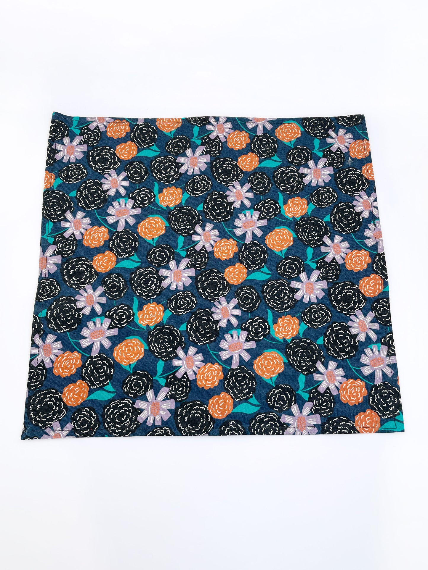 A navy blue pocket square with vivid orange, lavender, and black flowers, accented with fresh green leaves.