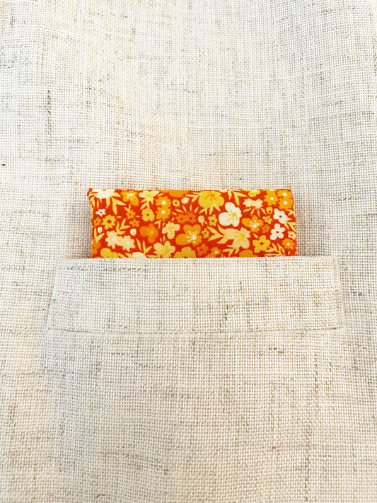 A handmade pocket square featuring vibrant orange and yellow flowers shown in the pocket of a suit jacket.